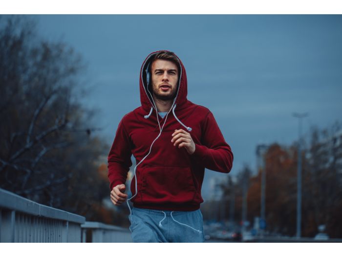 Man in red hoodie jogging beside the road in the city