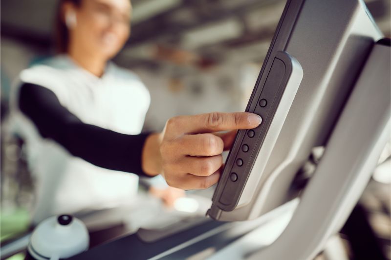 athletic woman adjusting speed on treadmill while exercising in a gym